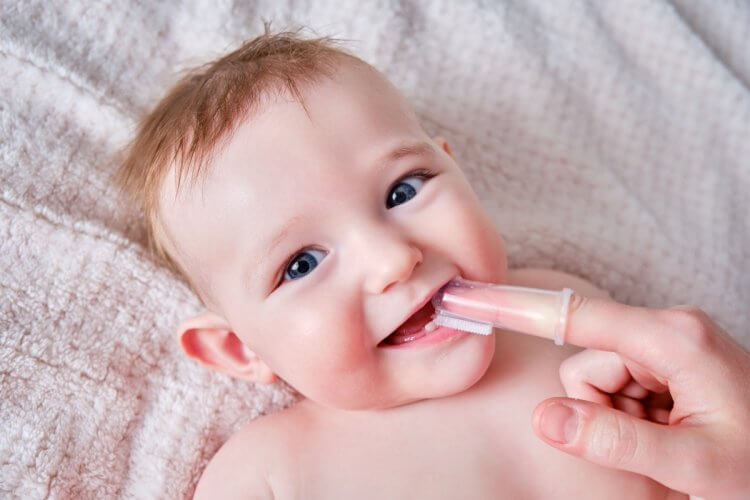 Mother Hands Brushing Teeth With A Finger Brush Of A Infant Baby