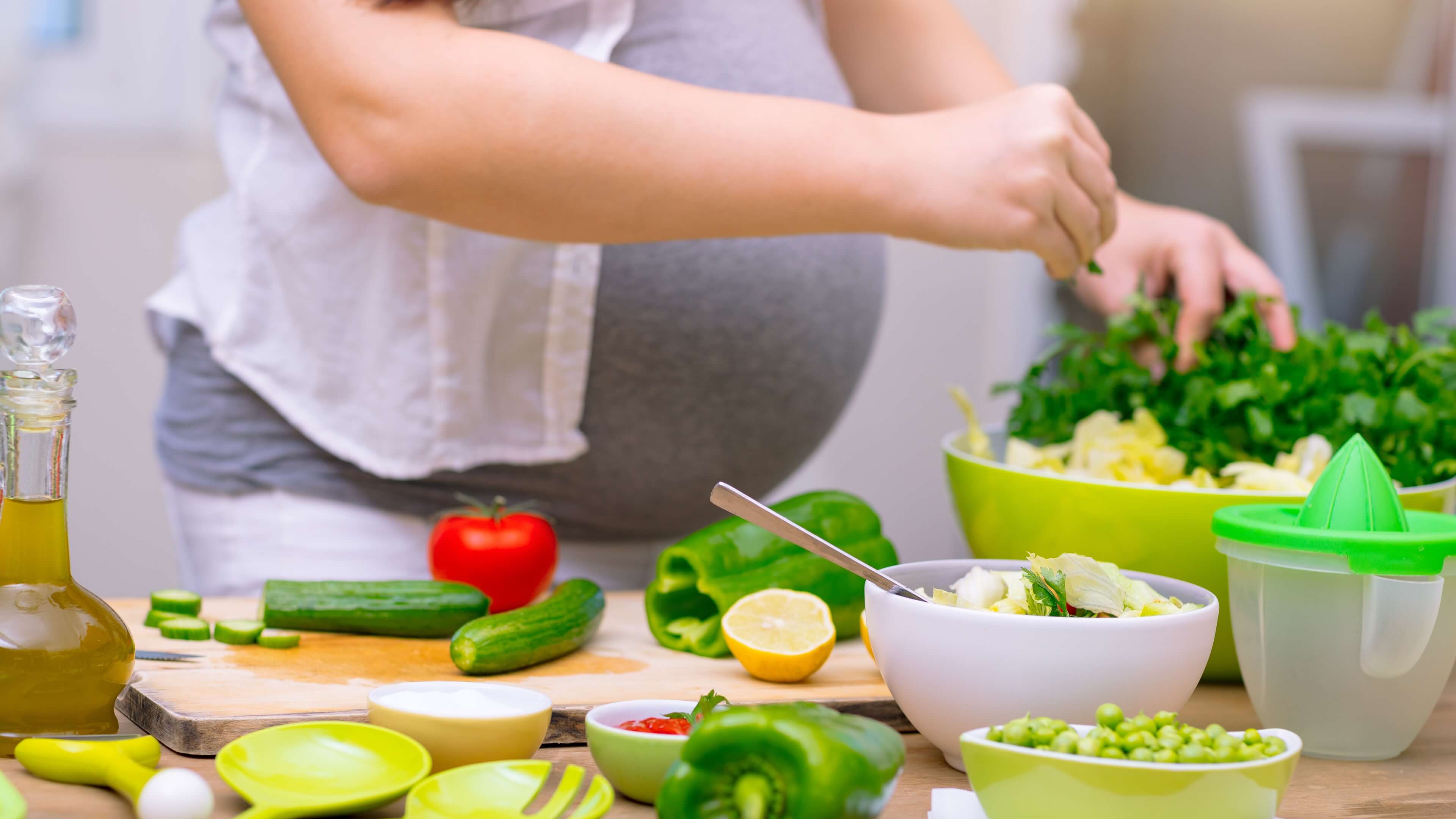 mujer embarazada vigilando su dieta y cocinando con tomates, pepinos, guisantes...